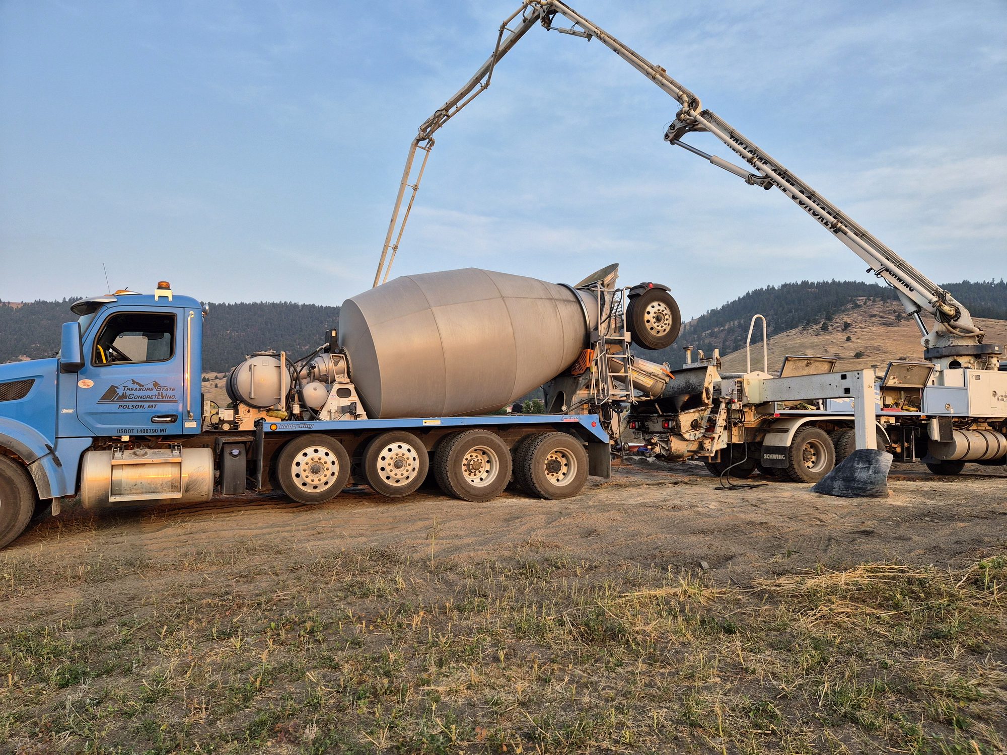 Blue Treasure State Concrete, Inc. mixer truck delivering concrete to a pump truck at a Montana jobsite